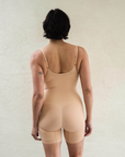 Sustainable shapewear. Back view of model wearing plant-based shapewear mid-thigh bodysuit in Ada nude, our lightest nude tone.Made from plant-based materials EVO and creora