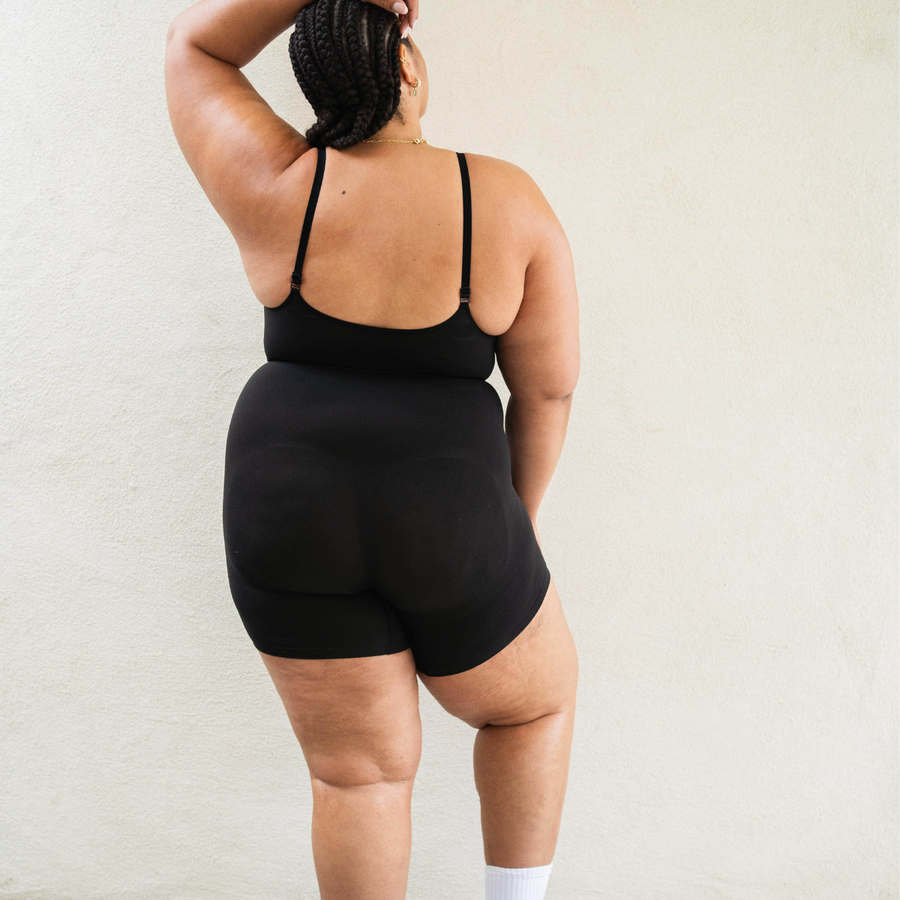 Sustainable shapewear back side of model in black plant-based shapewear mid-thigh bodysuit made from evo and creora