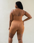 Sustainable shapewear. Model showing back of maya nude, a caramel medium nude tone, plant-based shapewear mid-thigh bodysuit. ethically and sustainably made in portugal. Made from bio-based Evo and creora