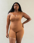 Sustainable shapewear. Model showing front of maya nude, a caramel medium nude tone, plant-based shapewear mid-thigh bodysuit. ethically and sustainably made in portugal. Made from bio-based Evo and creora