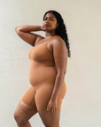 Sustainable shapewear. Side view of model in maya nude, a caramel medium nude tone, plant-based shapewear mid-thigh bodysuit. ethically and sustainably made in portugal. Made from bio-based Evo and creora