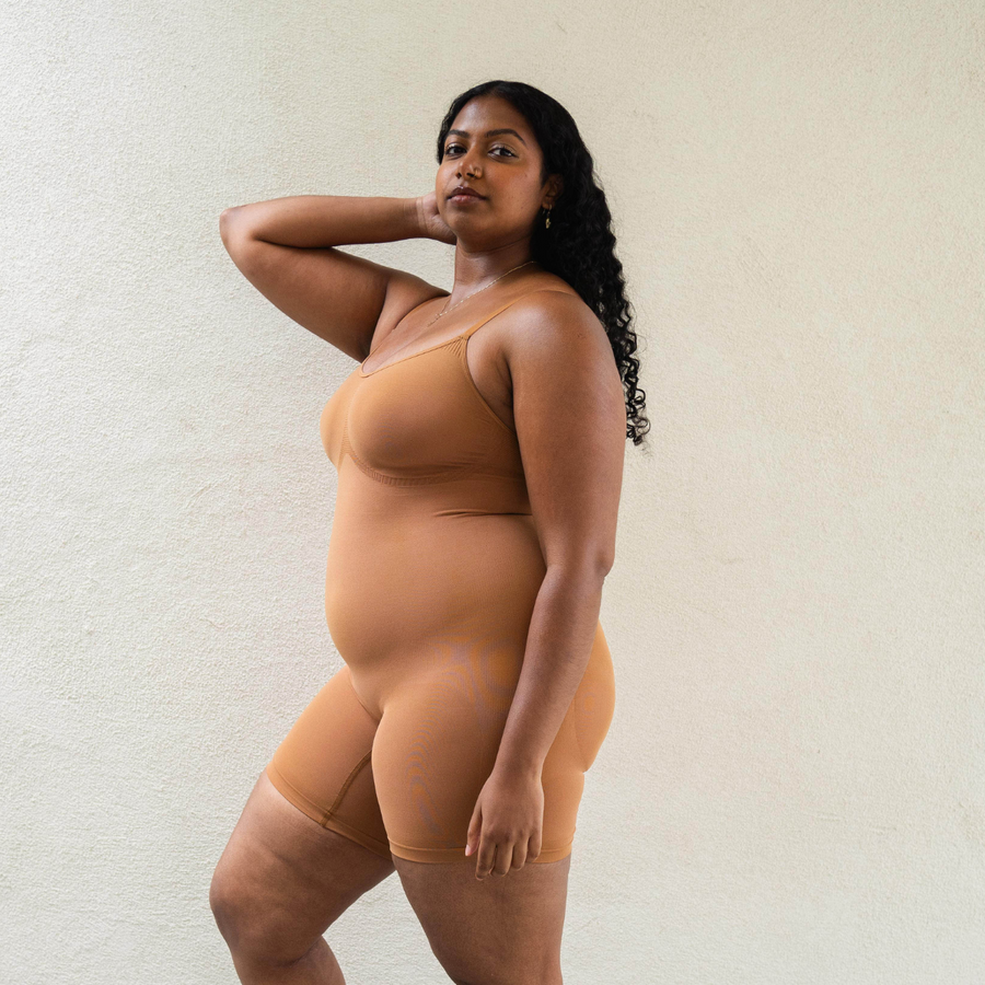 Sustainable shapewear. Side view of model in maya nude, a caramel medium nude tone, plant-based shapewear mid-thigh bodysuit. ethically and sustainably made in portugal. Made from bio-based Evo and creora