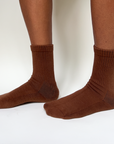 Model wearing a pair of organic pima cotton crew socks that are ethically and sustainably made in Peru. In Ella, a warm brown tone.