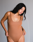 Model wearing maya nude, a caramel tone, bodysuit that is scoop neck style