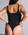 Back view of model wearing black bodysuit, thong style. 