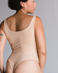 Back view of model in Ada nude, a beige tone, bodysuit. Scoop neck design. Thong style.